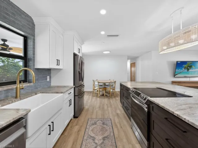 Kitchen featuring white cabinets, stainless steel appliances, light stone counters, backsplash, deep farm sink and recessed lighting