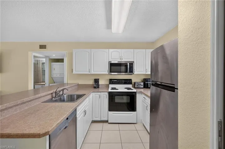 Kitchen featuring white cabinetry, a stainless steel refrigerator, a built-in microwave, and a double basin sink