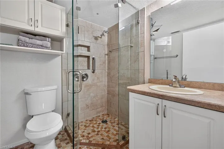 Glass-enclosed shower with a tiled surround, integrated shelving, and a mosaic tile floor