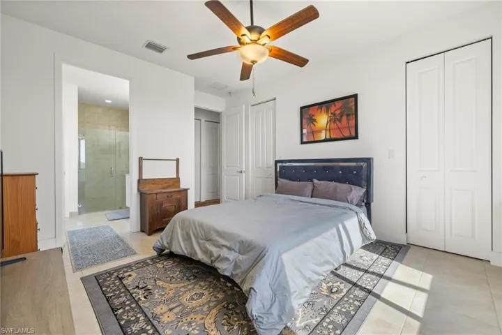 Bedroom featuring ceiling fan, light tile patterned floors, ensuite bathroom, and two closets
