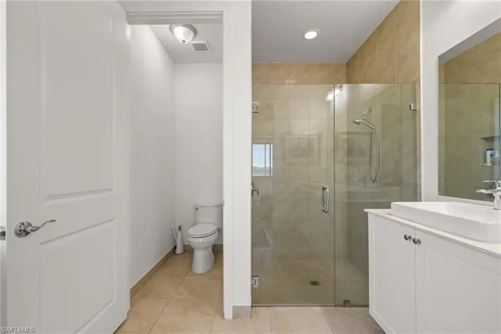 Bathroom with toilet, a shower with door, and tile patterned flooring