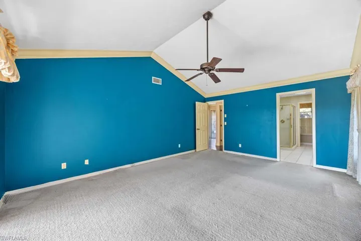 Unfurnished bedroom with light carpet, connected bathroom, lofted ceiling, and ceiling fan