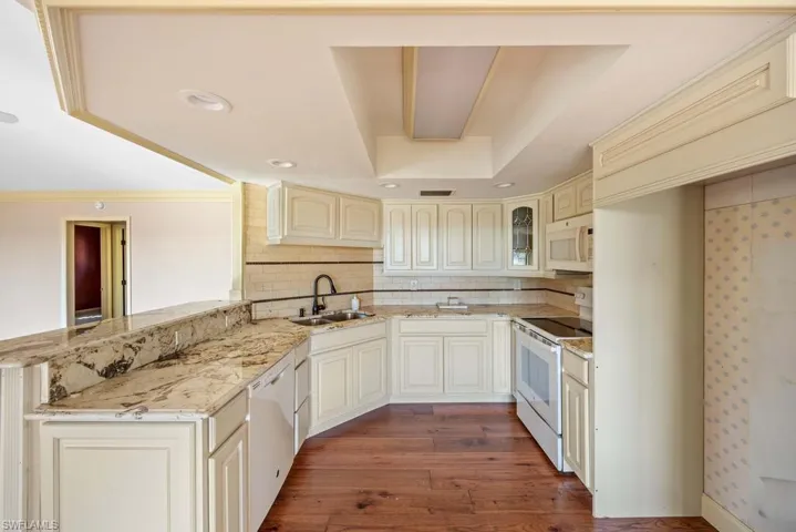 Kitchen with dark hardwood / wood-style floors, sink, light stone counters, kitchen peninsula, and white appliances