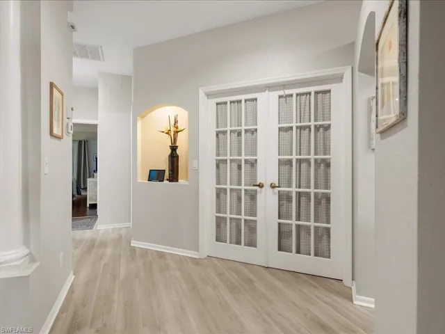 Double French doors with grid-patterned glass, light wood-finish flooring, recessed wall niche, arched doorway, and light wall paint throughout