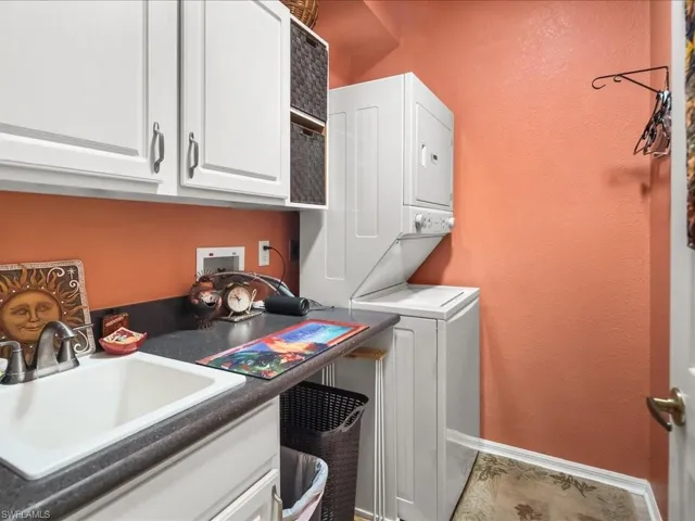 Laundry area featuring a utility sink, dark countertop, white cabinetry, and stacked appliances