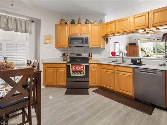 Kitchen featuring wood-finish cabinetry, stainless steel appliances, light-toned countertops, and a white subway tile backsplash