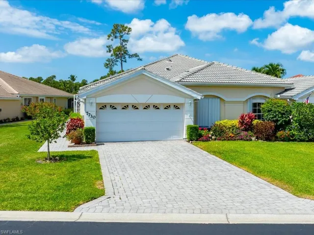 Exterior featuring a paver driveway, an attached two-car garage with transom window accents, a tiled roof, and established landscaping