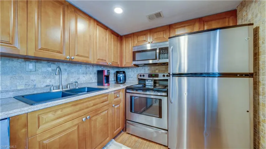 Kitchen with light stone countertops, sink, stainless steel appliances, and light hardwood / wood-style flooring