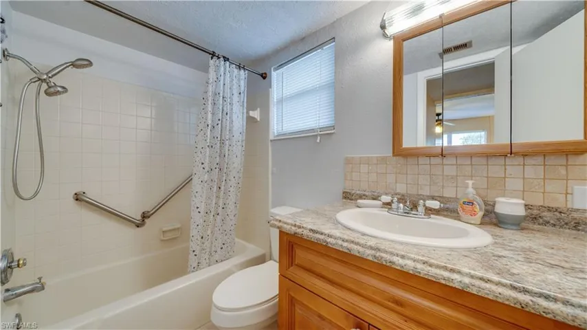 Full bathroom featuring vanity, shower / bath combo, textured backsplash, and toilet
