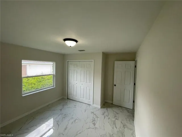 Unfurnished bedroom featuring light marble finish floors, baseboards, and a closet