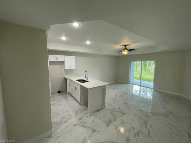 Kitchen with a sink, baseboards, a tray ceiling, recessed lighting, and white cabinets