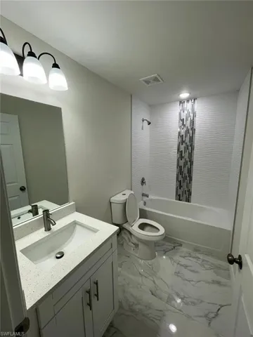 Bathroom with vanity, marble finish flooring, toilet, and bathing tub / shower combination