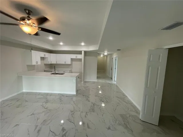 Kitchen featuring baseboards, a peninsula, a sink, a raised ceiling, and ceiling fan