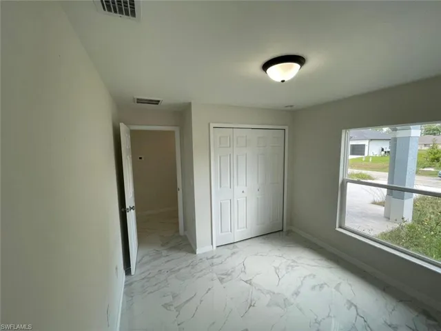 Unfurnished bedroom featuring light marble finish floors, baseboards, and multiple windows