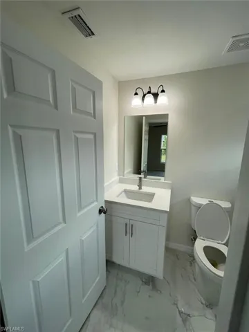Half bath with toilet, vanity, marble look tile flooring, and baseboards