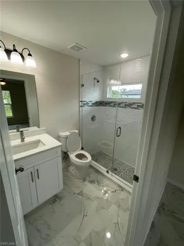 Bathroom featuring toilet, vanity, a stall shower, plenty of natural light, and recessed lighting
