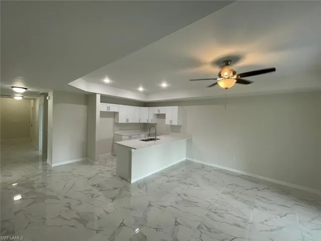 Kitchen with a tray ceiling, baseboards, a peninsula, a sink, and white cabinets