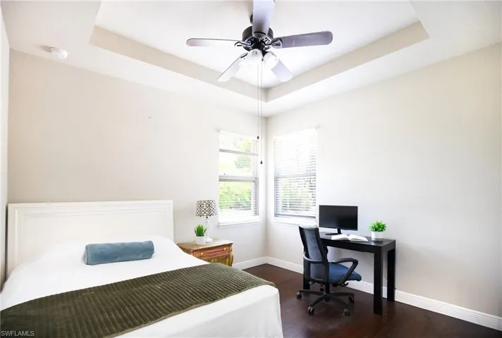 Bedroom with dark wood-type flooring, ceiling fan, and a raised ceiling