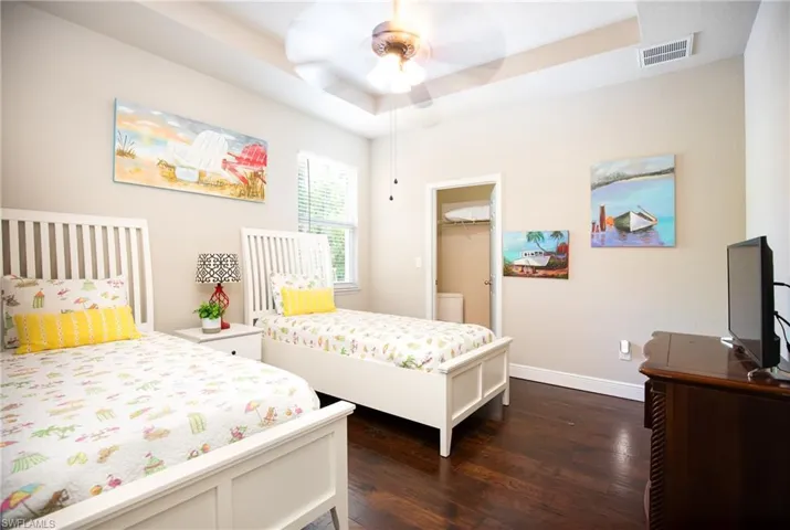 3rd Bedroom featuring a walk in closet, dark hardwood flooring, a tray ceiling, a closet, and ceiling fan