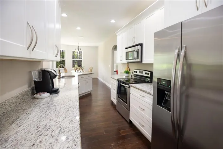 Kitchen with light stone countertops, stainless steel appliances, white cabinets, dark hardwood floors