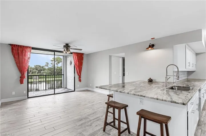 Kitchen featuring light wood-type flooring, a breakfast bar area, white cabinetry, ceiling fan, and light stone countertops