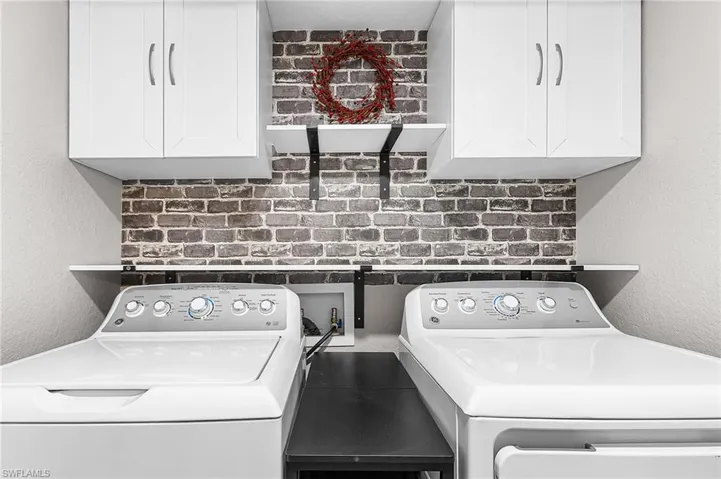 Laundry area featuring a textured wall, cabinet space, and washing machine and clothes dryer