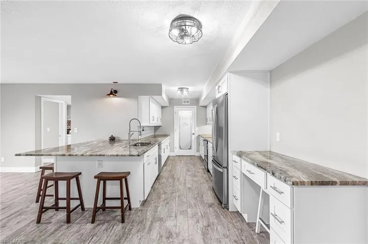 Kitchen with white cabinetry, light stone counters, a peninsula, a breakfast bar, and light wood finished floors