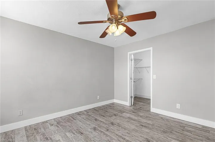 Unfurnished bedroom featuring a walk in closet, wood finished floors, and a ceiling fan