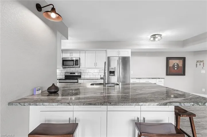 Kitchen with a kitchen breakfast bar, appliances with stainless steel finishes, white cabinetry, dark stone counters, and a textured wall