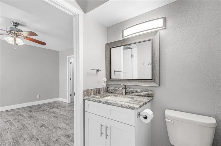 Half bathroom featuring vanity, light wood-style floors, a textured wall, and ceiling fan