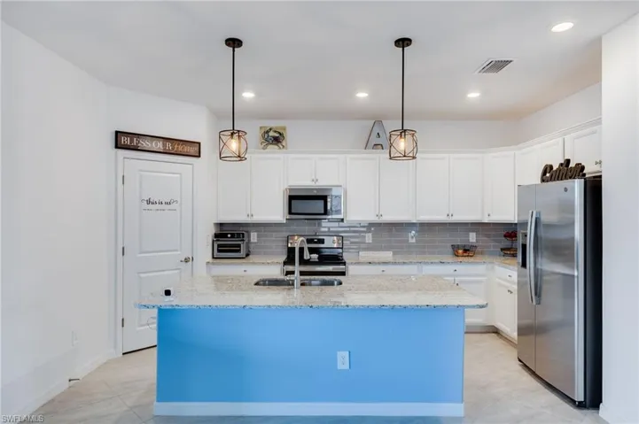 Kitchen with stainless steel appliances, hanging light fixtures, white cabinets, granite counters, and decorative backsplash