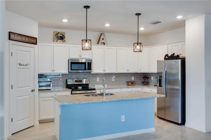 Kitchen with stainless steel appliances, hanging light fixtures, white cabinets, granite counters, and decorative backsplash