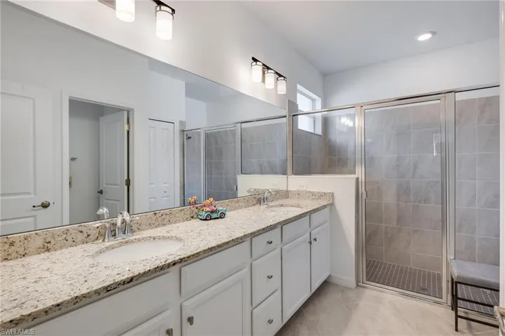 Primary bathroom with double vanity, a stall shower, and light tile patterned flooring