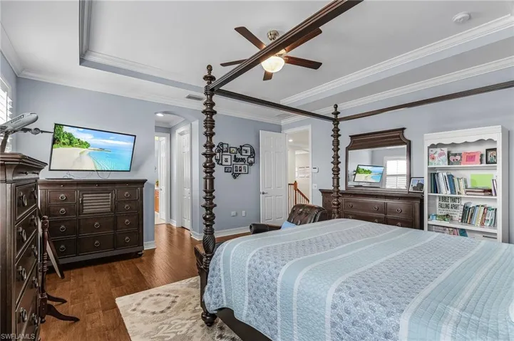 Bedroom with arched walkways, dark wood finished floors, ornamental molding, a ceiling fan, and a tray ceiling