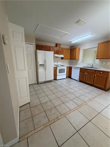 Kitchen featuring wood finish cabinetry, light countertops, white appliances, and light tile patterned floors