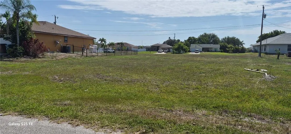 Expansive undeveloped lot featuring a grass cover and distant residential structures