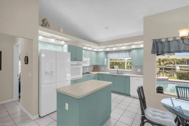Kitchen featuring white appliances, light tile patterned flooring, a kitchen island, and backsplash