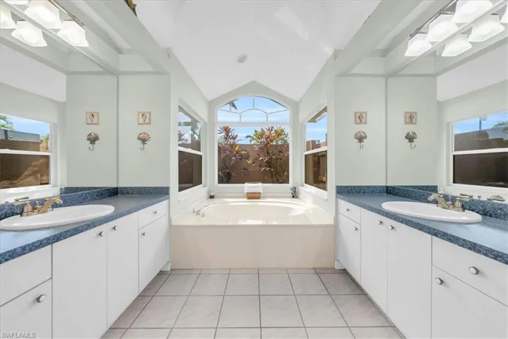 Bathroom with a garden tub, light tile patterned flooring, plenty of natural light, two vanities, and vaulted ceiling