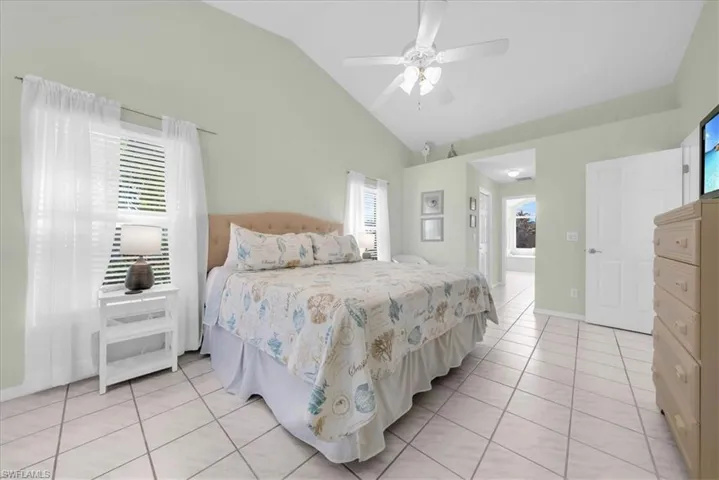Bedroom with light tile patterned floors, multiple windows, ceiling fan, and high vaulted ceiling