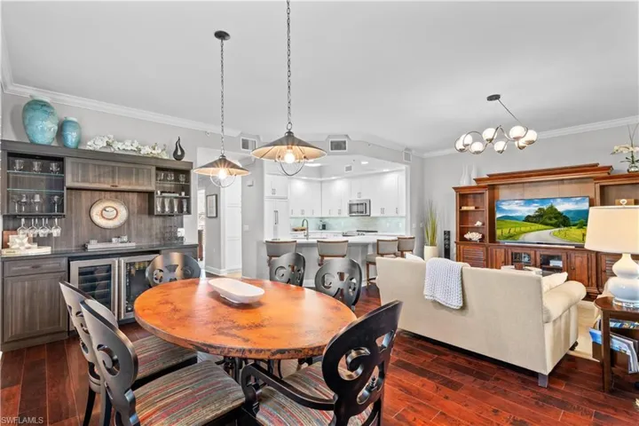Dining space with crown molding, dark wood-style flooring, a dry bar, a chandelier, and wine cooler
