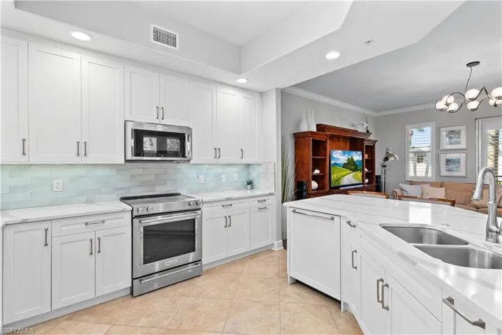 Kitchen with white cabinets, stainless steel appliances, ornamental molding, open floor plan, and recessed lighting