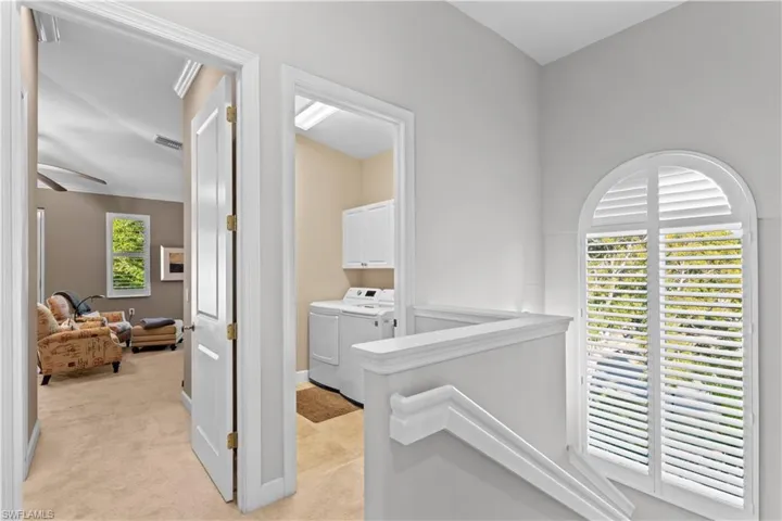 Corridor featuring light colored carpet, washing machine and clothes dryer, and an upstairs landing
