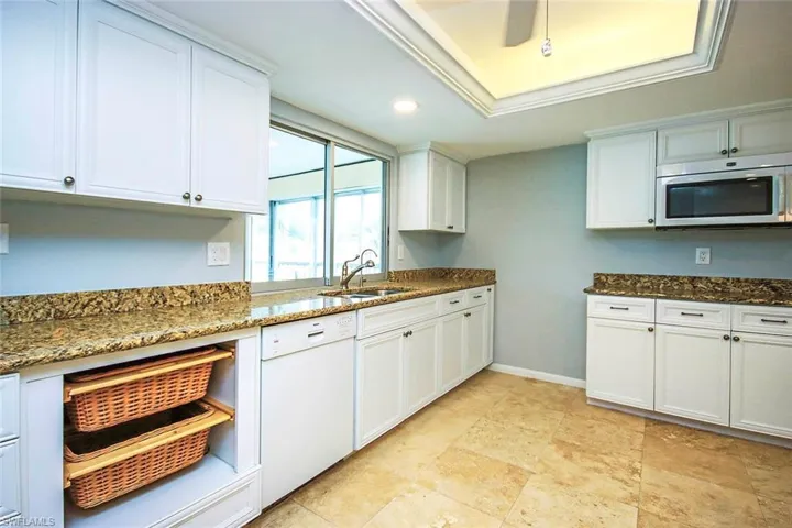 Kitchen featuring white cabinetry, stainless steel microwave, dark stone countertops, a sink, and dishwasher