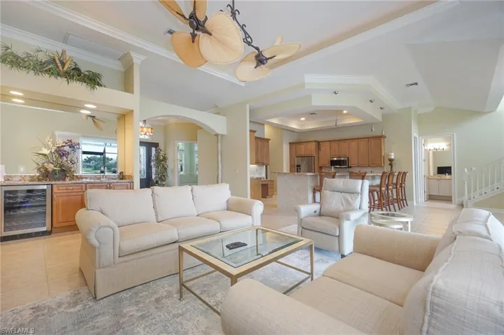 Living area with light tile patterned flooring, beverage cooler, a raised ceiling, crown molding, and arched walkways