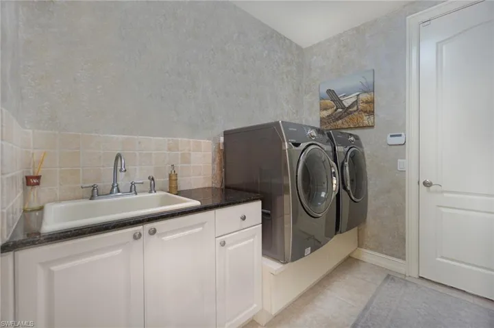 Clothes washing area featuring cabinet space, light tile patterned floors, separate washer and dryer, and a sink
