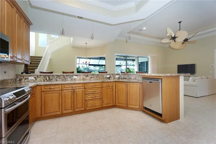 Kitchen featuring stainless steel appliances, brown cabinets, open floor plan, light stone countertops, and crown molding