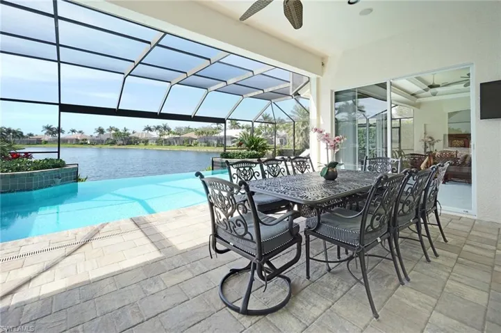 Outdoor pool featuring a ceiling fan, glass enclosure, a water view, and a patio