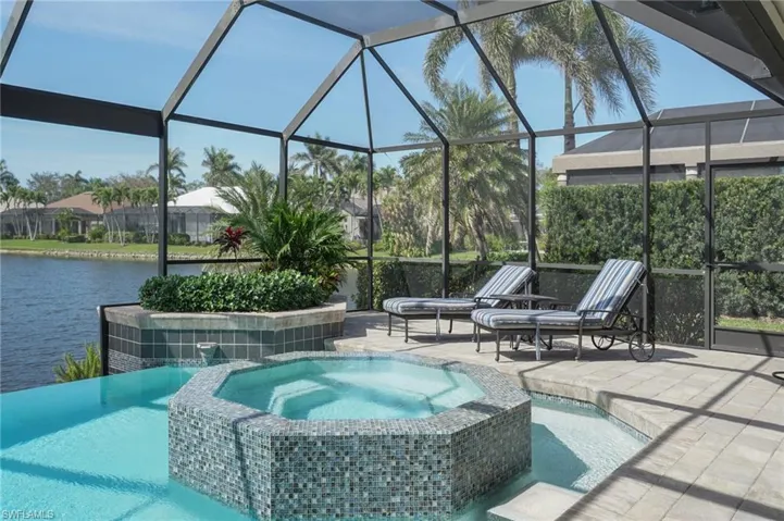 View of pool with a patio area, glass enclosure, a water view, and a pool with connected hot tub