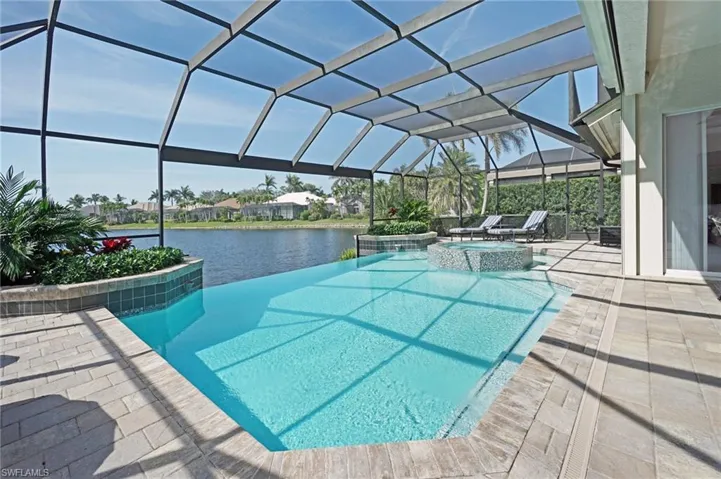 View of swimming pool with a lanai, a water view, a pool with connected hot tub, and a patio