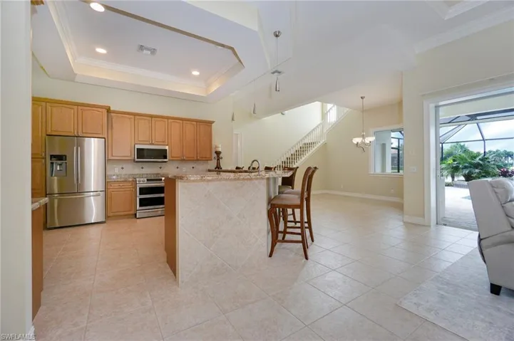 Kitchen with crown molding, stainless steel appliances, a raised ceiling, light tile patterned floors, and a breakfast bar area